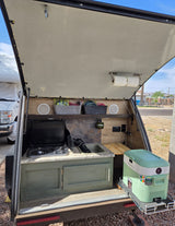 This organized teardrop RV rental's outdoor kitchen features a stove, sink, speakers, and a convenient pull-out cooler for camping.