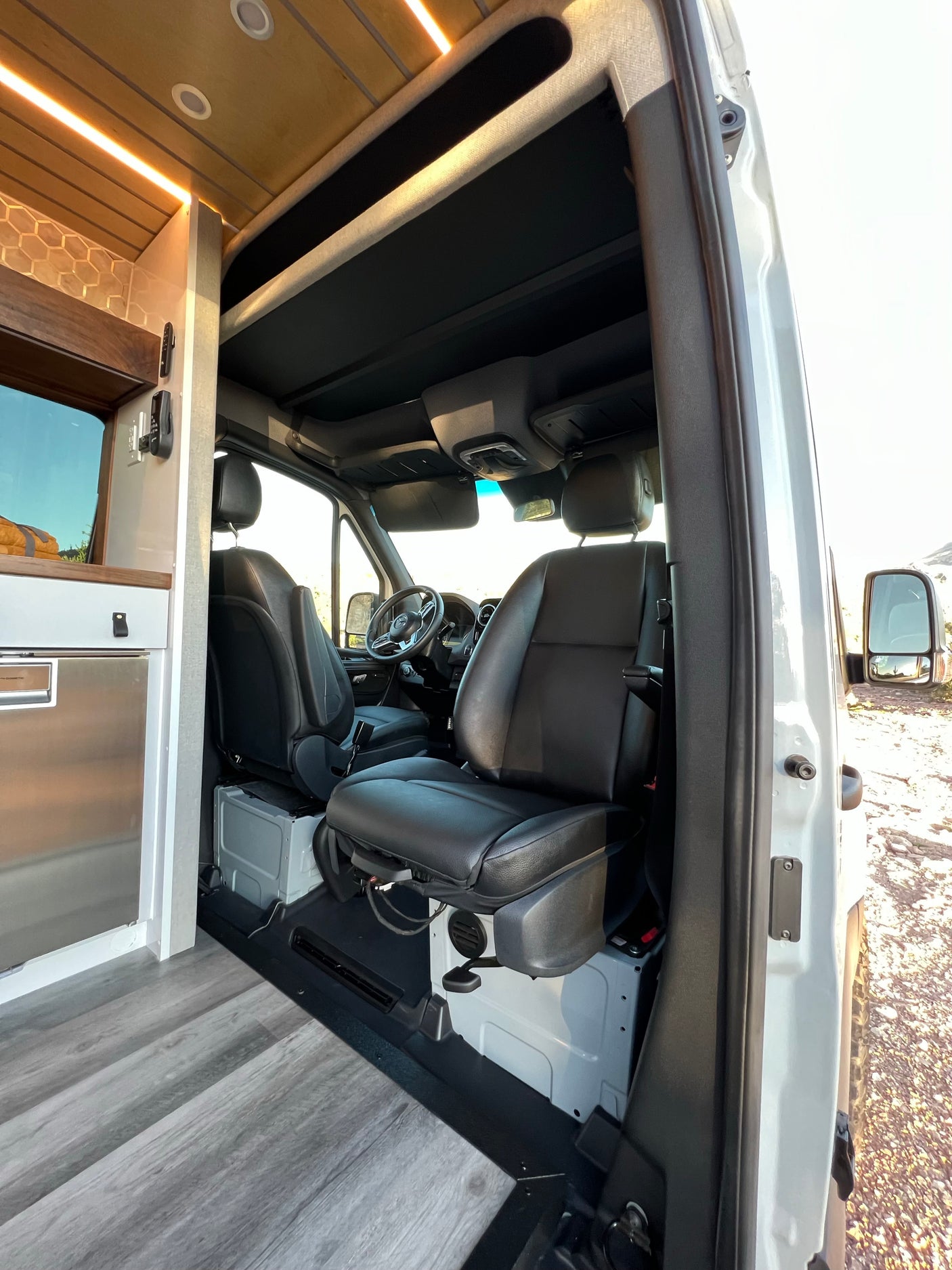 Spacious rv rental interior: custom kitchen with Dometic fridge, wood ceiling, and driver's cabin with leather seats.