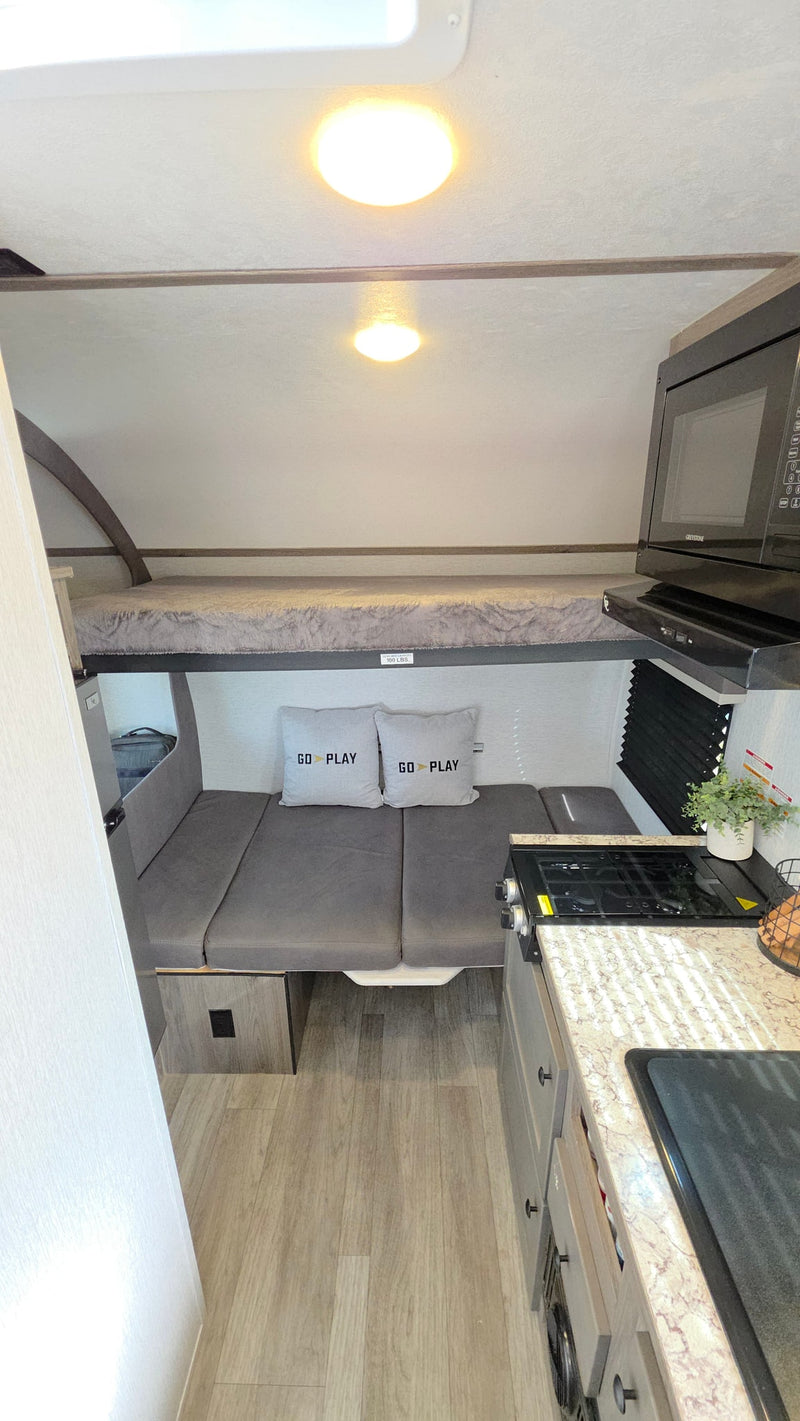 Cozy rv rental interior featuring a bunk bed, a dinette area with "GO PLAY" pillows, and a compact kitchen. — photo 7