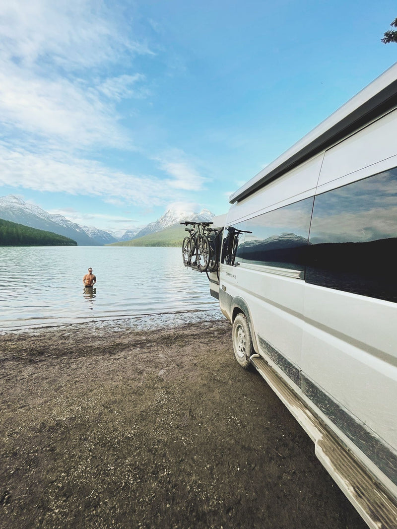  and a striped blanket facing a scenic nature view. (THOR RV visible).|Modern silver RV rental van with a pop-top roof extended — photo 4