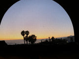 Golden sunset over ocean, silhouetted palm trees, viewed from an RV rental through a screen. A beautiful travel sight.