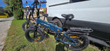 Two Jasion fat-tire electric bikes lean against a white RV rental van, parked on grass by a sidewalk for outdoor fun.