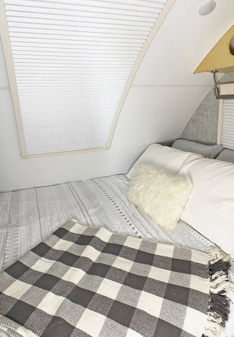 Cozy RV rental bedroom with white bedding, a fluffy pillow, and black & white plaid blanket.