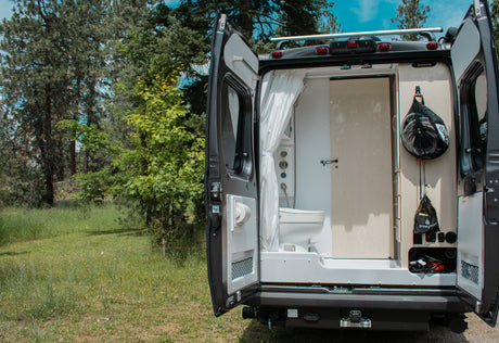 RV rental van's open rear doors show a compact shower, toilet, and utility storage. Ready for your next outdoor adventure.