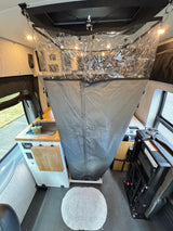RV rental interior: clear-top shower with gray fabric walls, compact sink, and seating area.