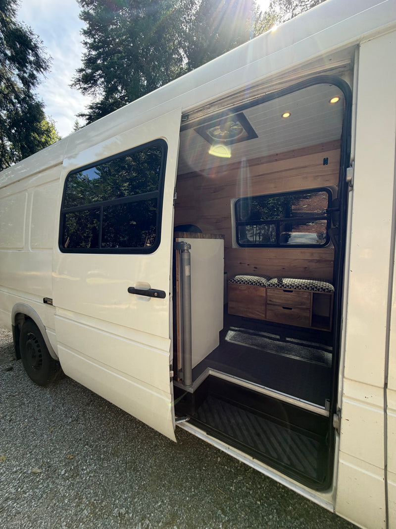 Open side door of a white camper van showing a custom wood interior, bench seat, and drawers. A perfect RV rental choice! — photo 3