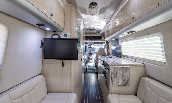 Step inside this bright rv rental! Modern interior with a kitchen, seating, & wall-mounted TV. — photo 14