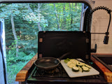 Cooking fresh zucchini in an RV rental kitchen with a beautiful forest view. Ideal for nature lovers & camping trips.