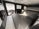 Inviting rv rental interior: large gray bed/couch, light carpet, AC, and bunks. Ready for your camping journey.