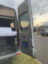 Open RV rental rear reveals a cozy bed and storage. Perfect for van life adventures.