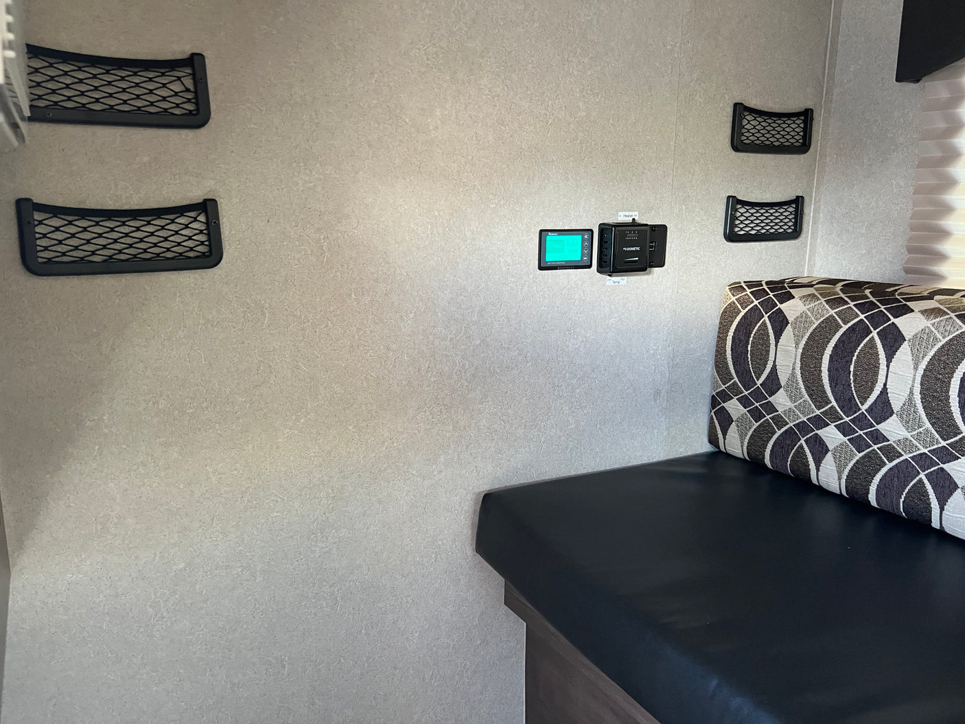 RV rental interior featuring wall-mounted mesh storage, a Dometic heater/temp control, and battery monitor above a bench seat.