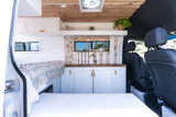 Interior of a modern camper van RV rental with a cozy bed, stylish kitchen, and natural wood accents. Perfect for travel.