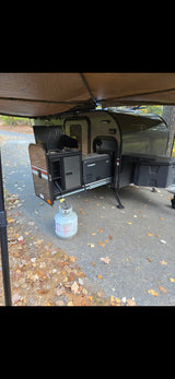 RV rental: outdoor kitchen with Dometic cooler and propane tank under an extended awning on a paved campsite.