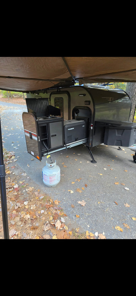 RV rental: outdoor kitchen with Dometic cooler and propane tank under an extended awning on a paved campsite.