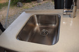 Inside an RV rental: a gleaming stainless steel sink with a chrome faucet and light speckled countertop, showing a view outdoors.