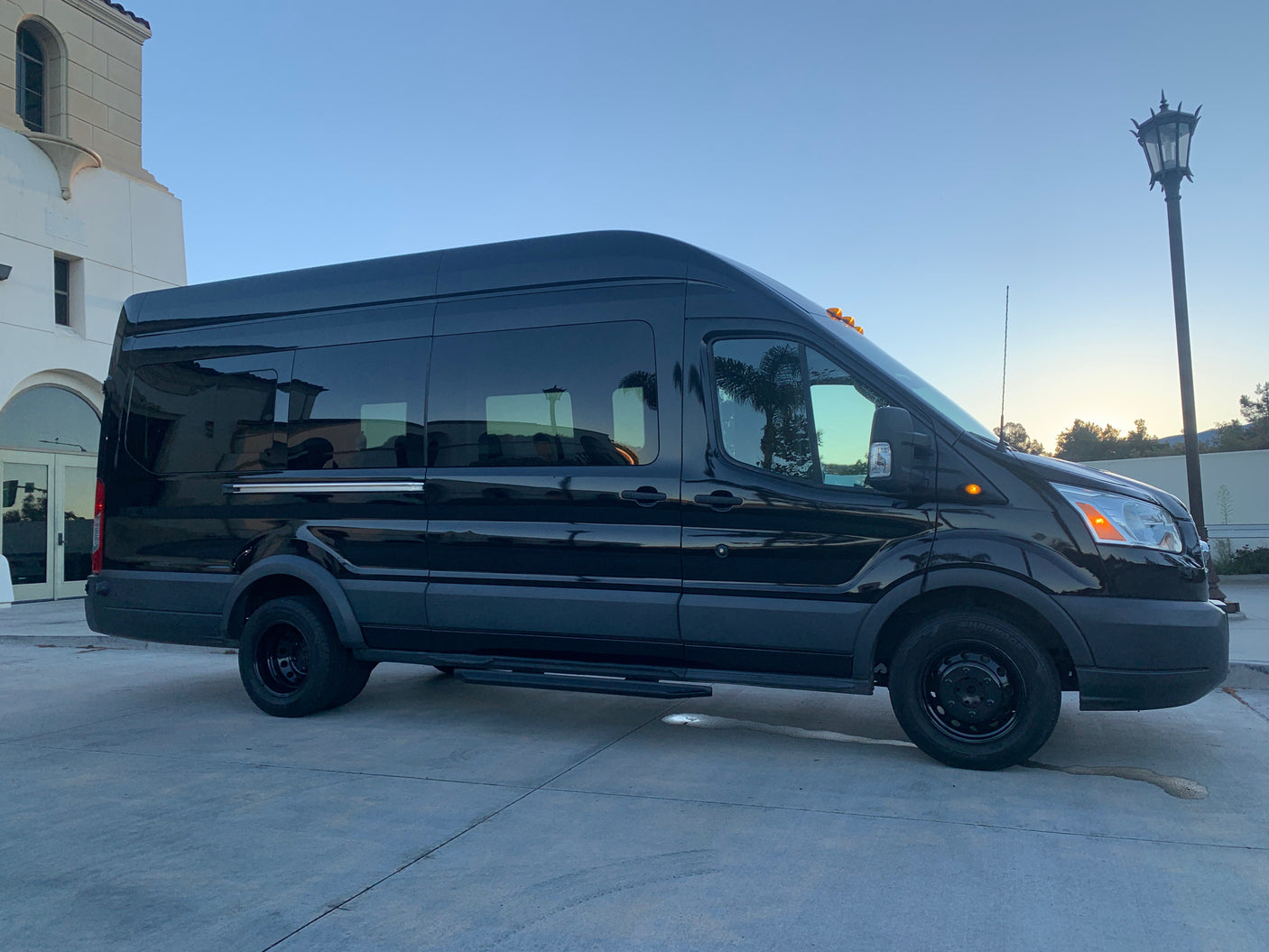 Black luxury passenger van, ideal for travel or RV rental, parked on concrete outside a building.