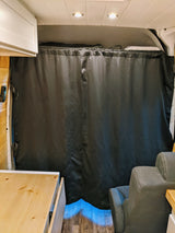 RV rental interior. A large black privacy curtain separates the rear, complemented by white cabinets, wood paneling, and a grey seat.