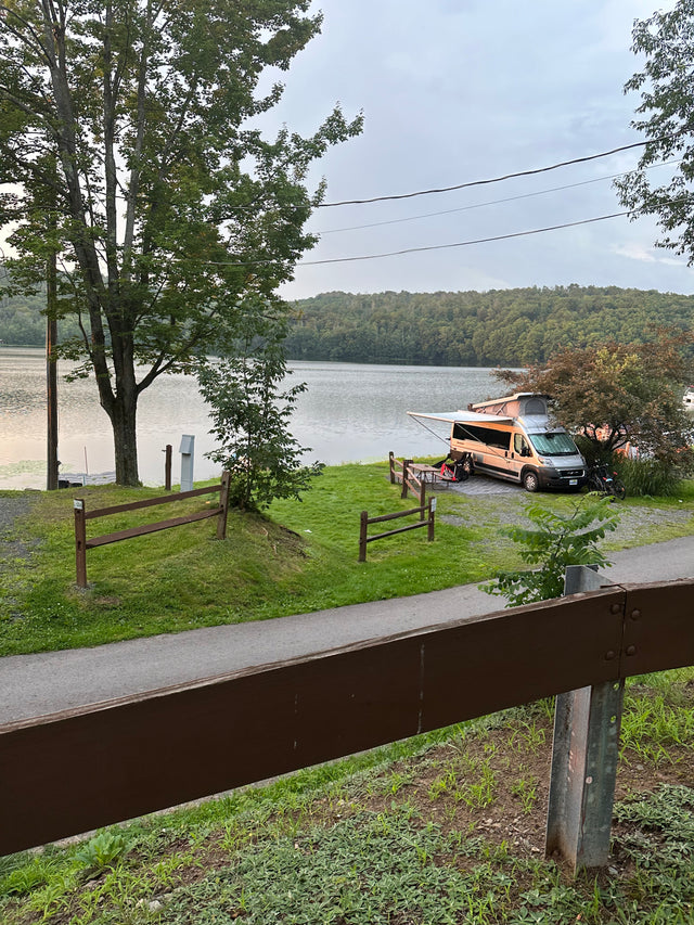 An RV rental parked lakeside at a serene campsite, surrounded by lush forest. Perfect outdoor escape.