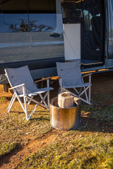 RV rental setup: Two camping chairs await a cozy evening around a Solo Stove fire pit beside a parked camper van.