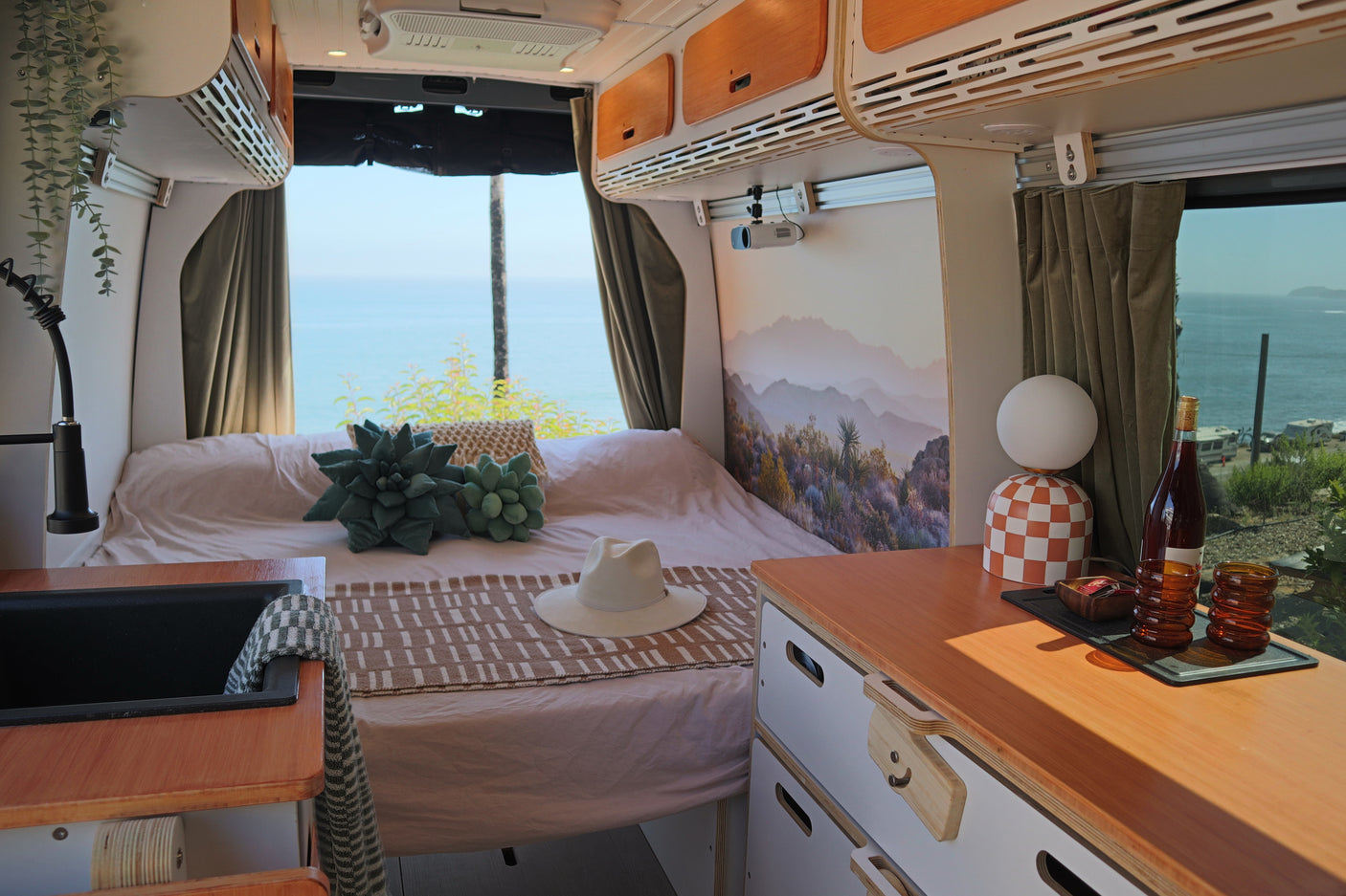 RV rental interior: cozy bed, desert mural, ocean views. Features a kitchen sink, projector & stylish storage for travel.