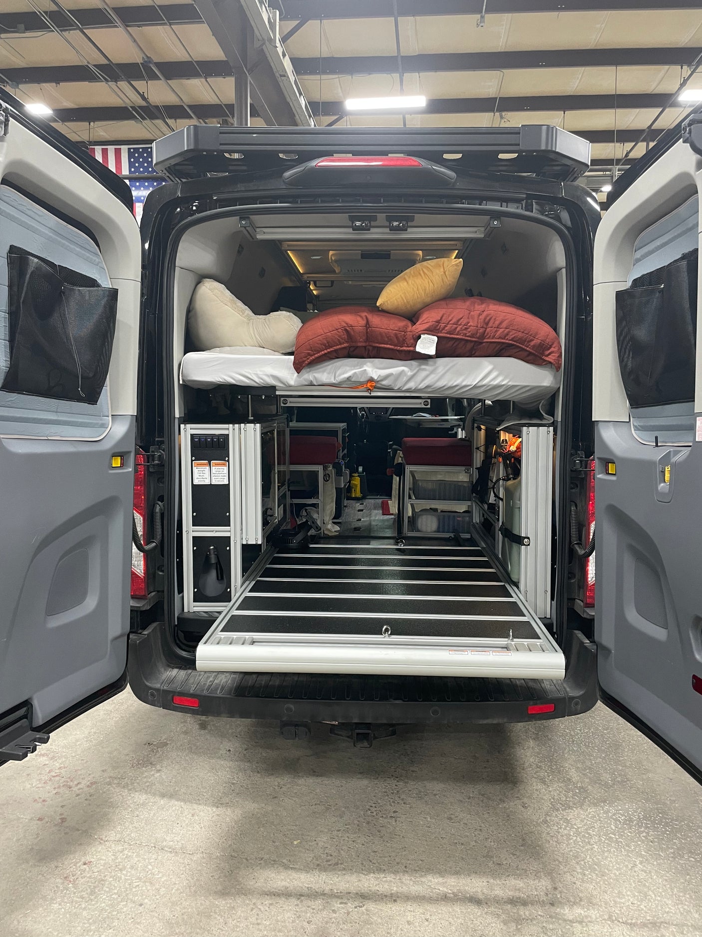 Inside an RV rental camper van: elevated bed, modular storage, and a pull-out ramp at the rear for easy access.