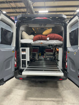 Inside an RV rental camper van: elevated bed, modular storage, and a pull-out ramp at the rear for easy access.