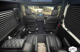 This luxury RV rental features a spacious custom van interior with black quilted leather captain's chairs, window blinds, & driver's cockpit view.