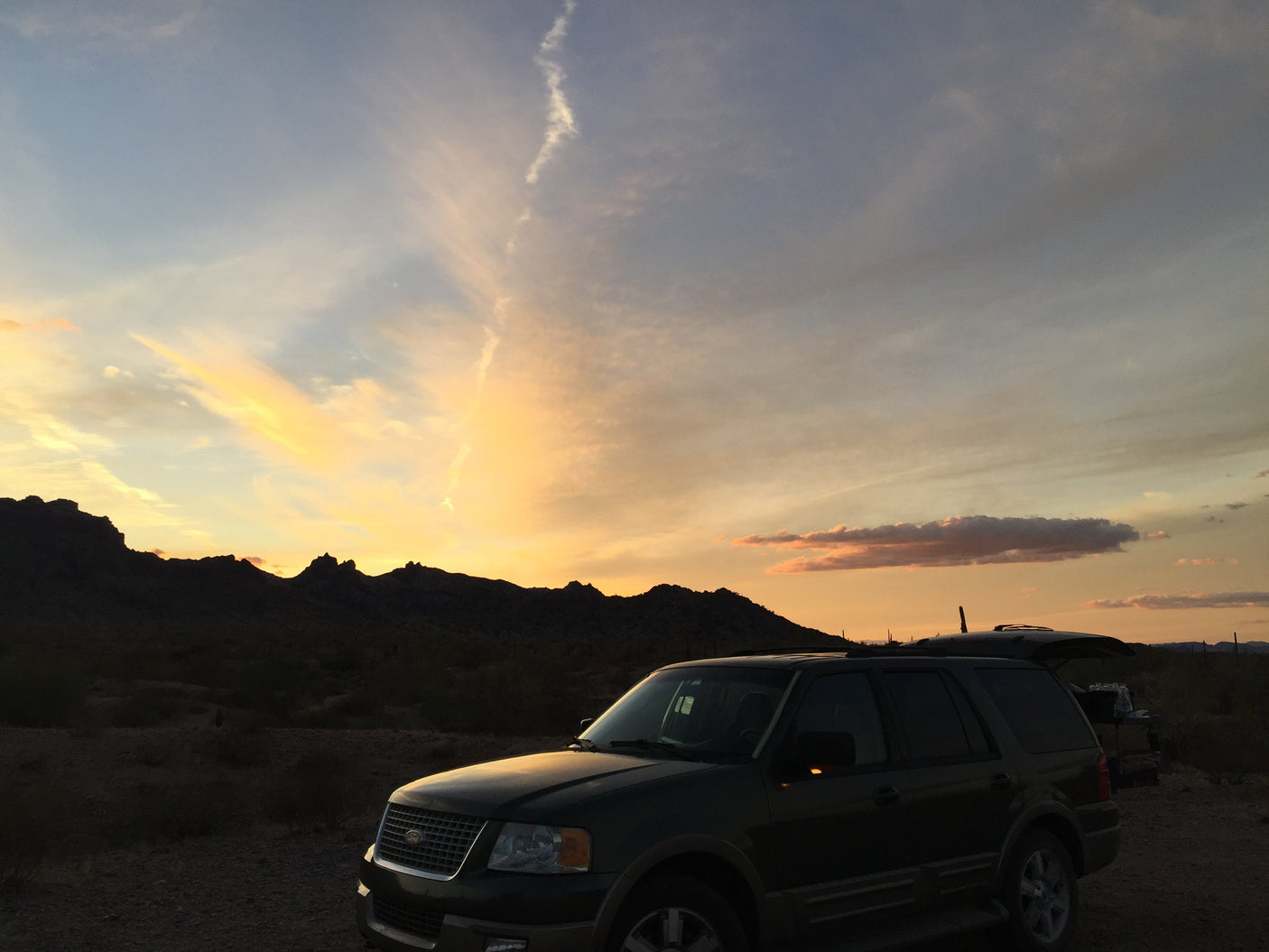 SUV parked under a vibrant desert sunset and mountains. Ideal for outdoor getaways, consider an RV rental for longer trips.