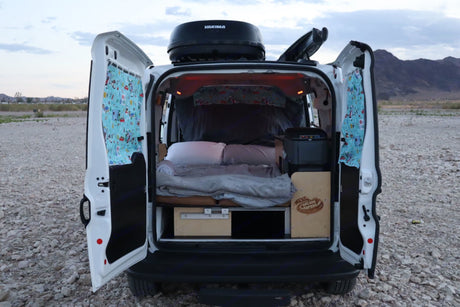 This RV rental offers cozy van life: open rear reveals a bed, storage, and a Yakima cargo box, ready for adventure.