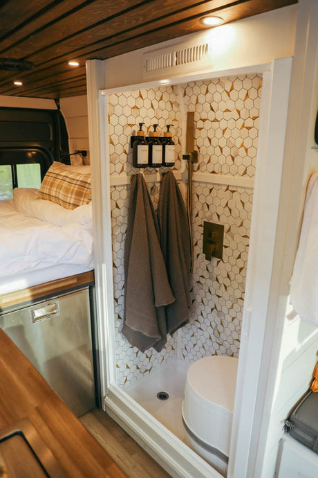 Inside this modern RV rental: a comfortable bed, integrated fridge, and a compact bathroom with hexagonal tiled shower.