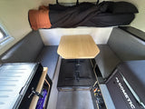 RV rental interior: elevated bed, central dinette with table & benches, plus portable stove & Dometic cooler.