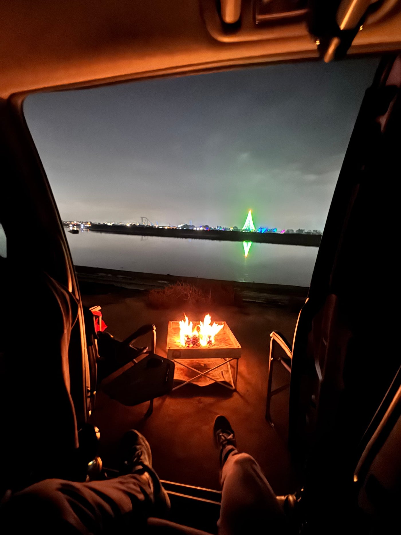 Cozy night view from an **rv rental**: feet up, fire pit blazing, city lights reflecting on the water. — photo 13