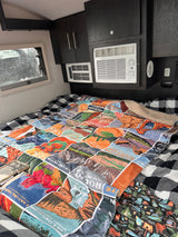RV rental interior: cozy bed with buffalo check and National Park blanket, plus built-in AC units and dark cabinets.
