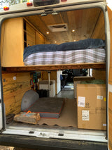Inside this cozy RV rental: a wooden interior with a raised bed, visible power setup, and an adjustable table in its box, ready for use.