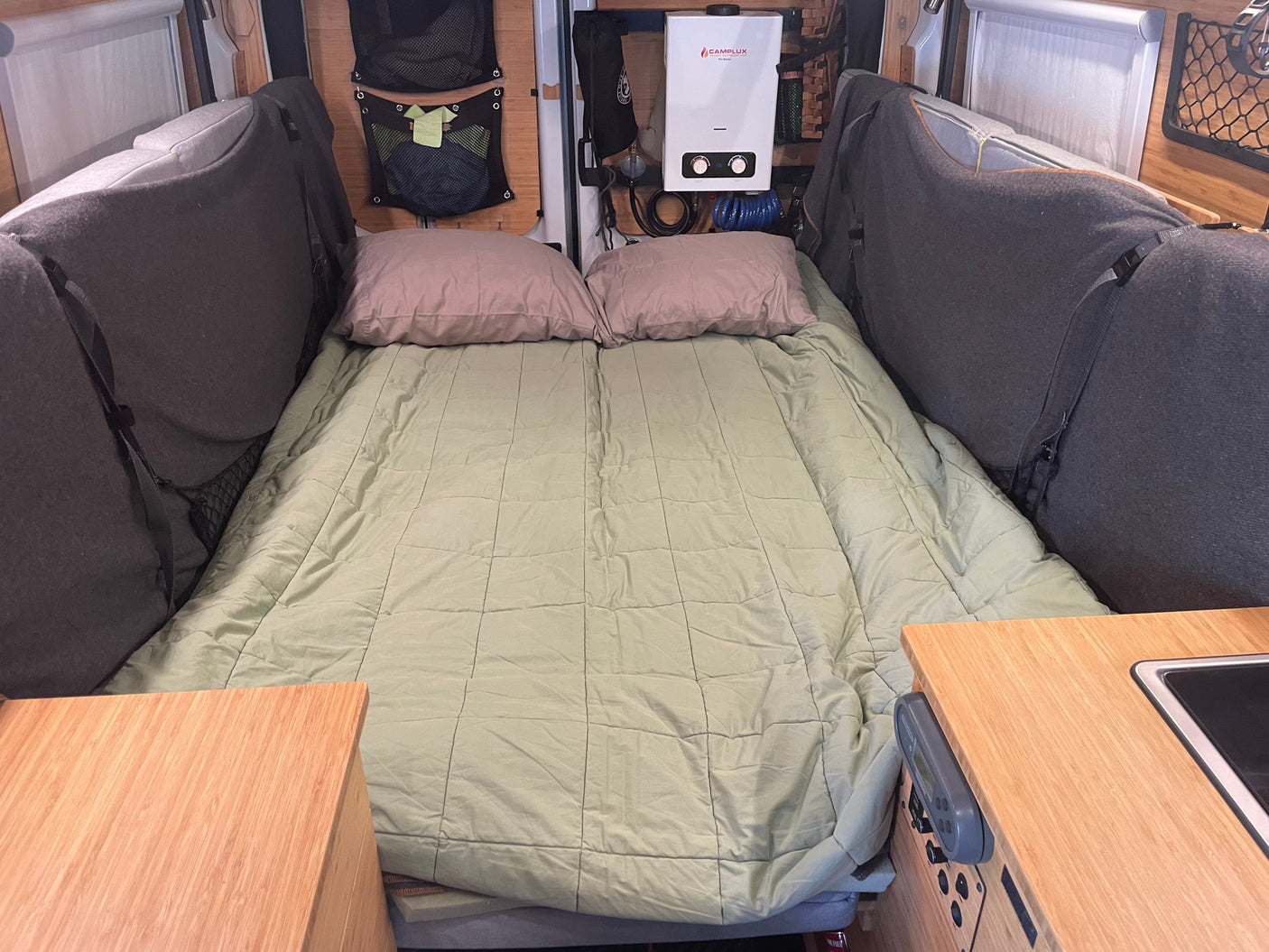 Inside a spacious RV rental: a neatly arranged bed, soft pillows, and essential amenities like a water heater and compact kitchen.