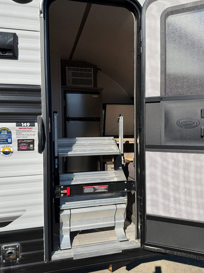 Open door of an rv rental revealing interior with folded steps, AC, and refrigerator. — photo 6
