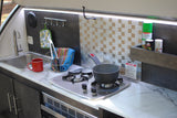 An RV rental kitchenette features a sink, two-burner stove with a pot, and counter space for compact travel cooking.