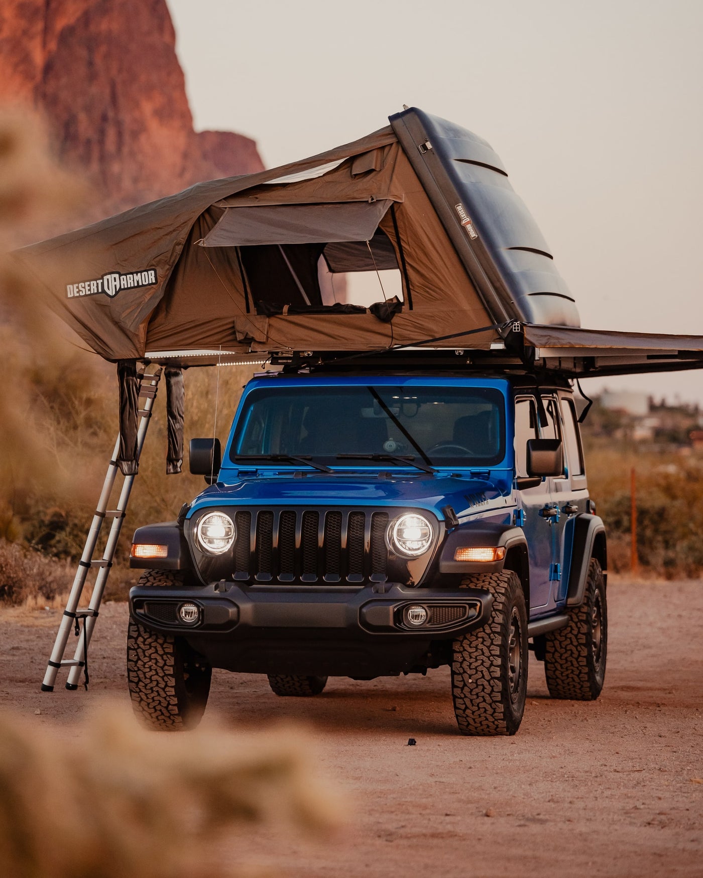 A blue Jeep Wrangler with a Desert Armor rooftop tent deployed, ladder extended. Great for an RV rental off-road camping adventure. — photo 7