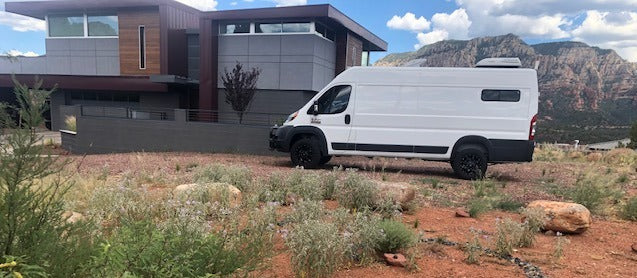 Explore with an RV rental! This white camper van is parked by a modern home, set against majestic red rock mountains. — photo 12