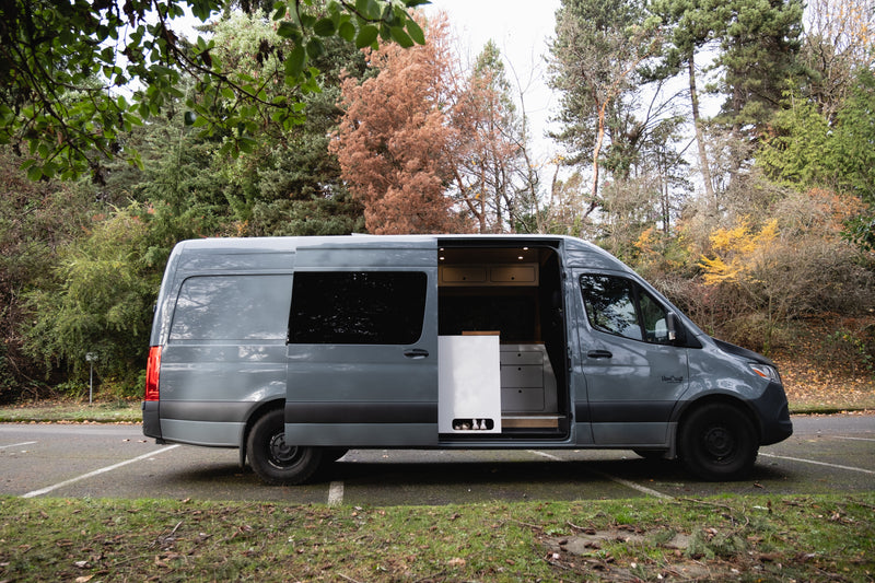 A grey camper van, a perfect RV rental, parked in a lot, with its side door open, revealing a light-colored, functional interior. — photo 19