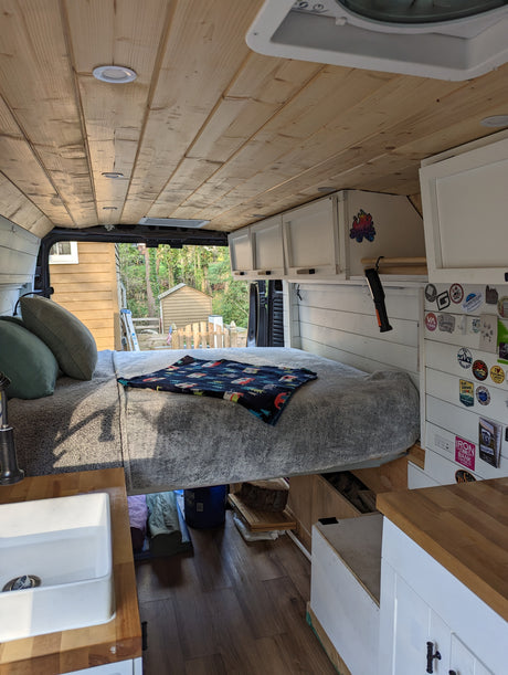Explore this inviting RV rental: a camper van interior with a comfy bed, compact sink, wood ceiling, and outdoor views.
