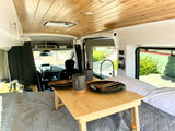 This RV rental's cozy camper van interior features a bed with a dining tray, kitchenette, and wooden ceiling.