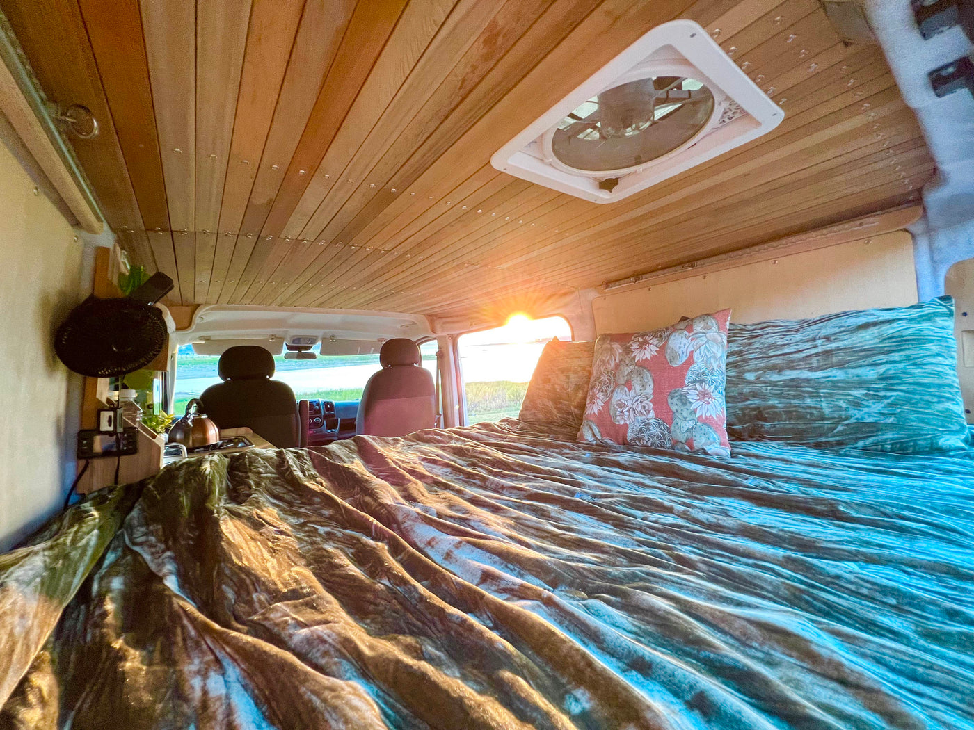 **RV rental** camper van interior: warm wooden ceiling, inviting bed, and sunset glow from the windshield. — photo 6