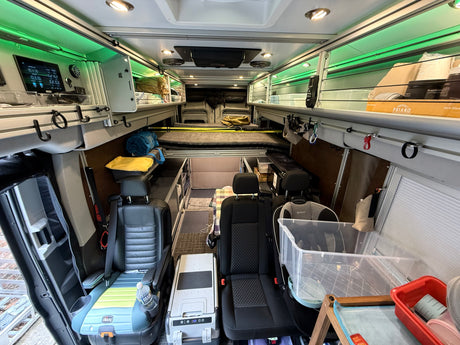 This RV rental interior features a functional van conversion with front seating, a child booster, a bed, and extensive storage with green LED lighting.