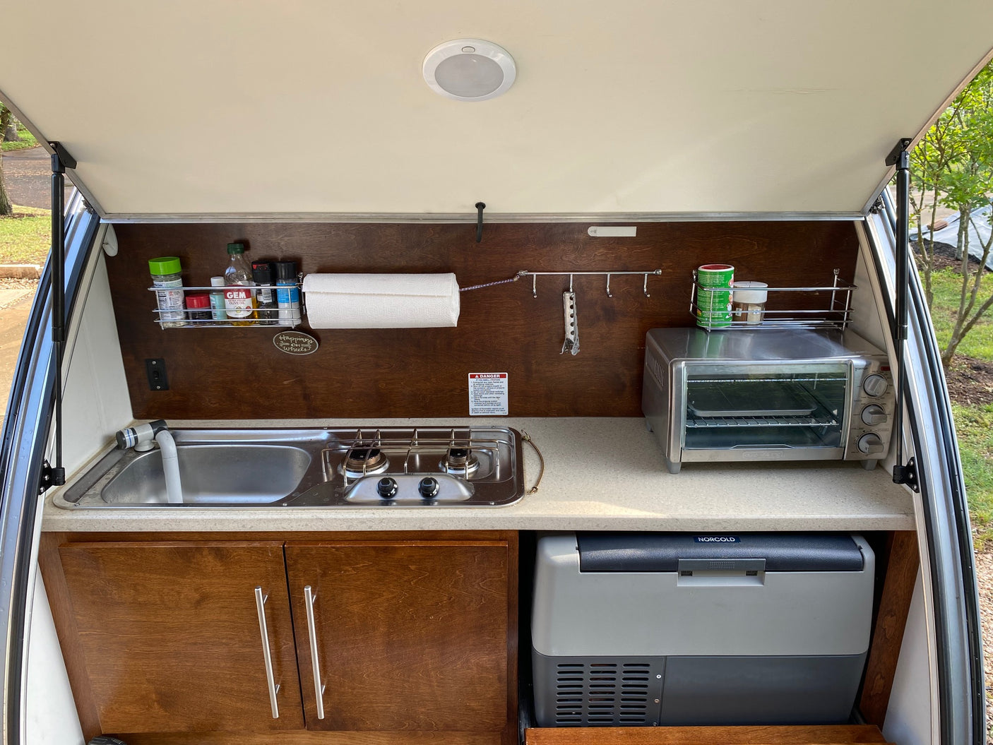Compact RV rental outdoor kitchen with sink, stove, toaster oven, and portable fridge.