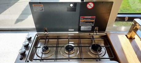 RV rental kitchen: Stainless steel 3-burner gas stove, sink, and wooden cutting board in a compact camper interior.