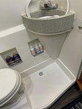 Compact RV rental wet bath with toilet, corner sink, shower, and recessed shelves for toiletries.