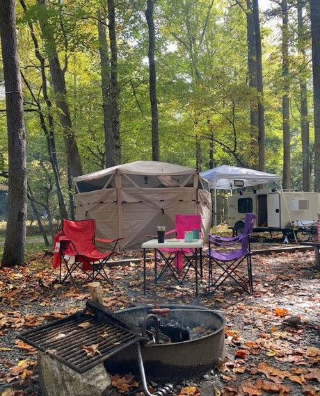 Enjoying an RV rental in the autumn forest! Our campsite includes a teardrop camper, pop-up tent, chairs, and a fire pit.
