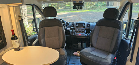Inside an RV rental: front cabin with seats, dash, and a cozy table. Ready for a scenic road trip adventure.