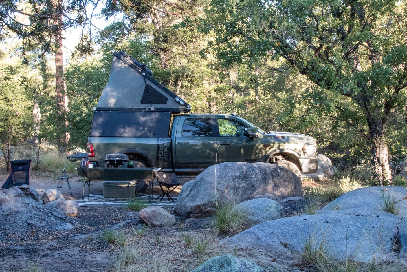 Rugged truck with pop-top camper parked in a rocky forest campsite. A perfect rv rental for your next overland adventure!